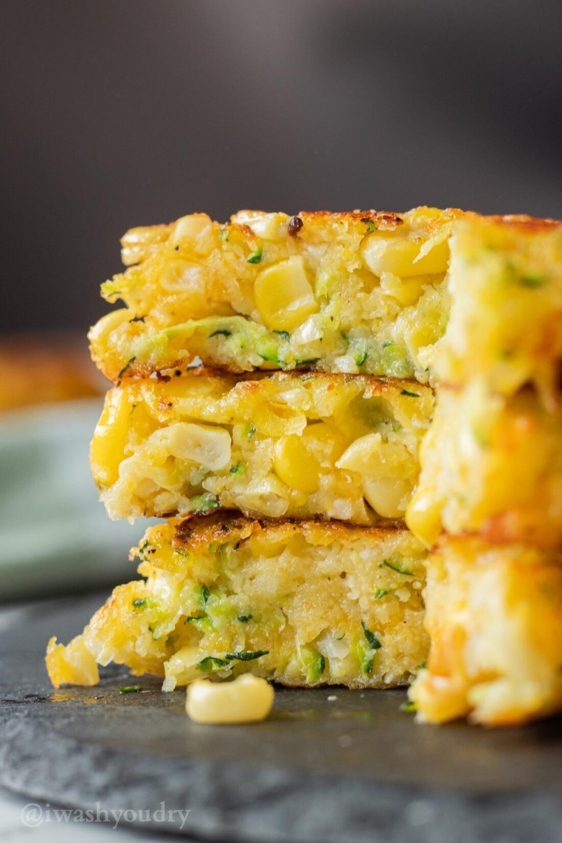 3 sliced zucchini corn fritters on black slate. 