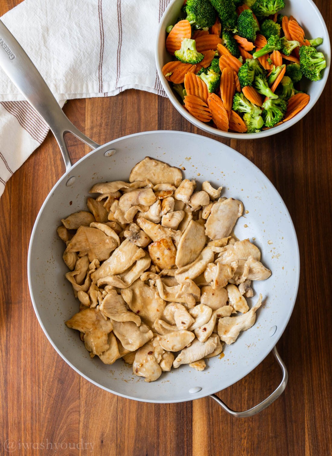 Cooked chicken in pan on wood board with bowl of vegetables. 