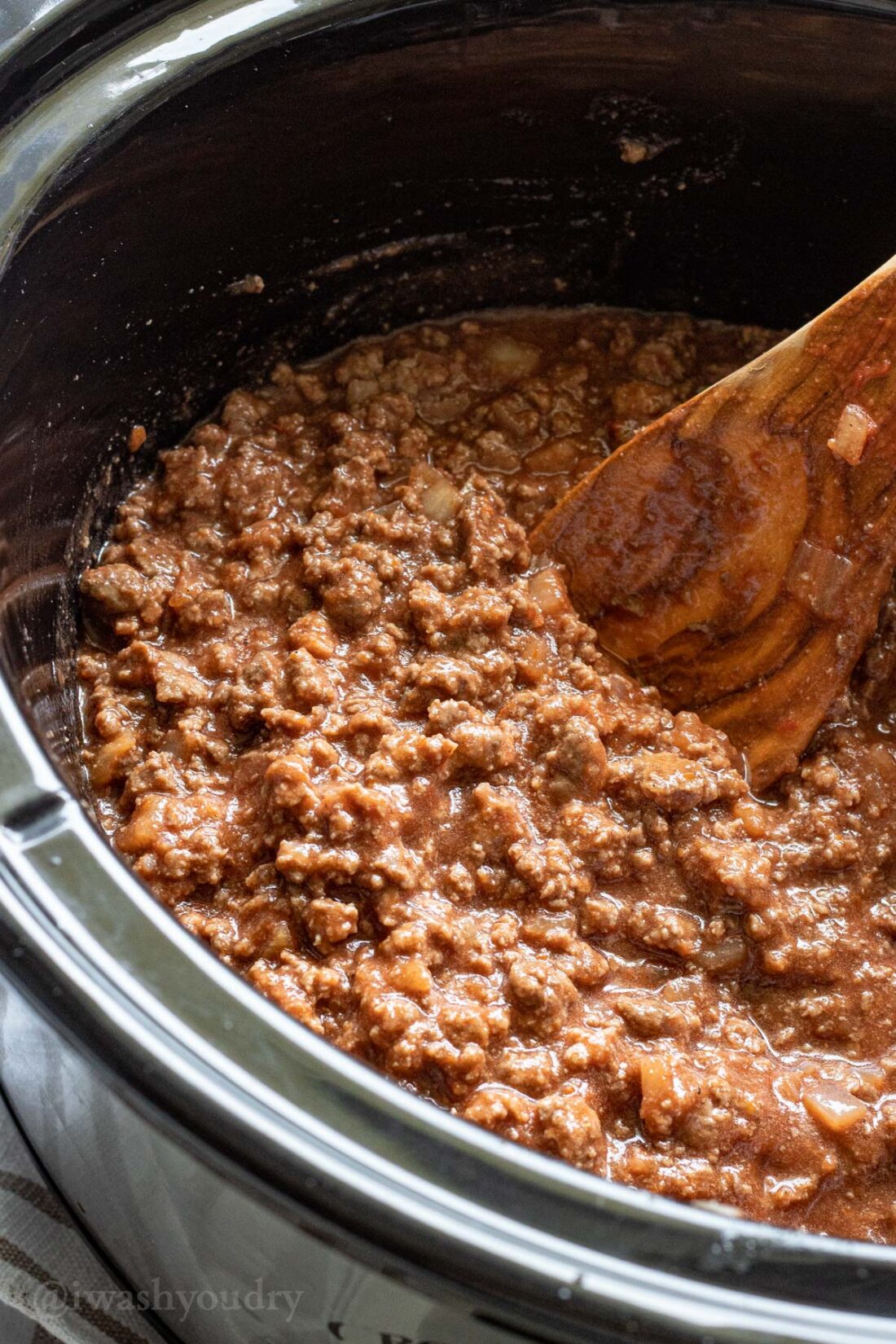 Sloppy Joe cooked in a black slow cooker with a spoon. 