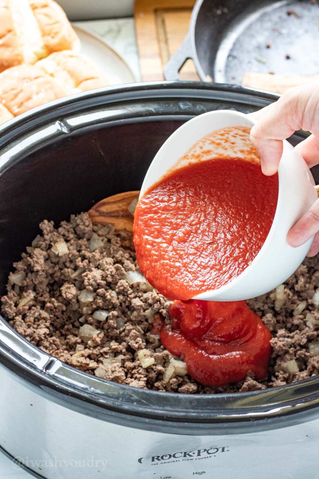 Pour a white bowl of tomato sauce into a slow cooker with ground beef.