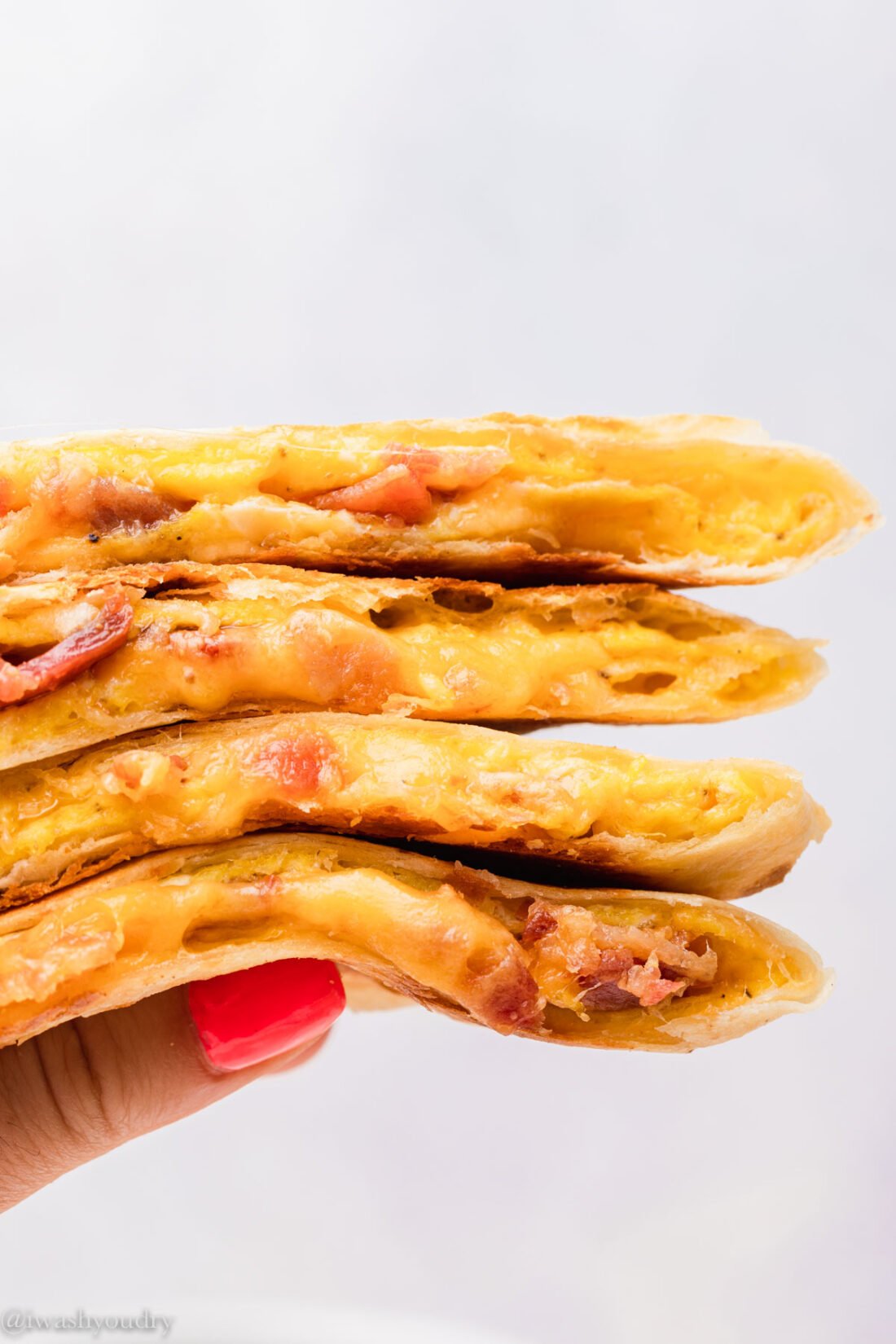 Hand holding stack of cooked breakfast quesadillas.