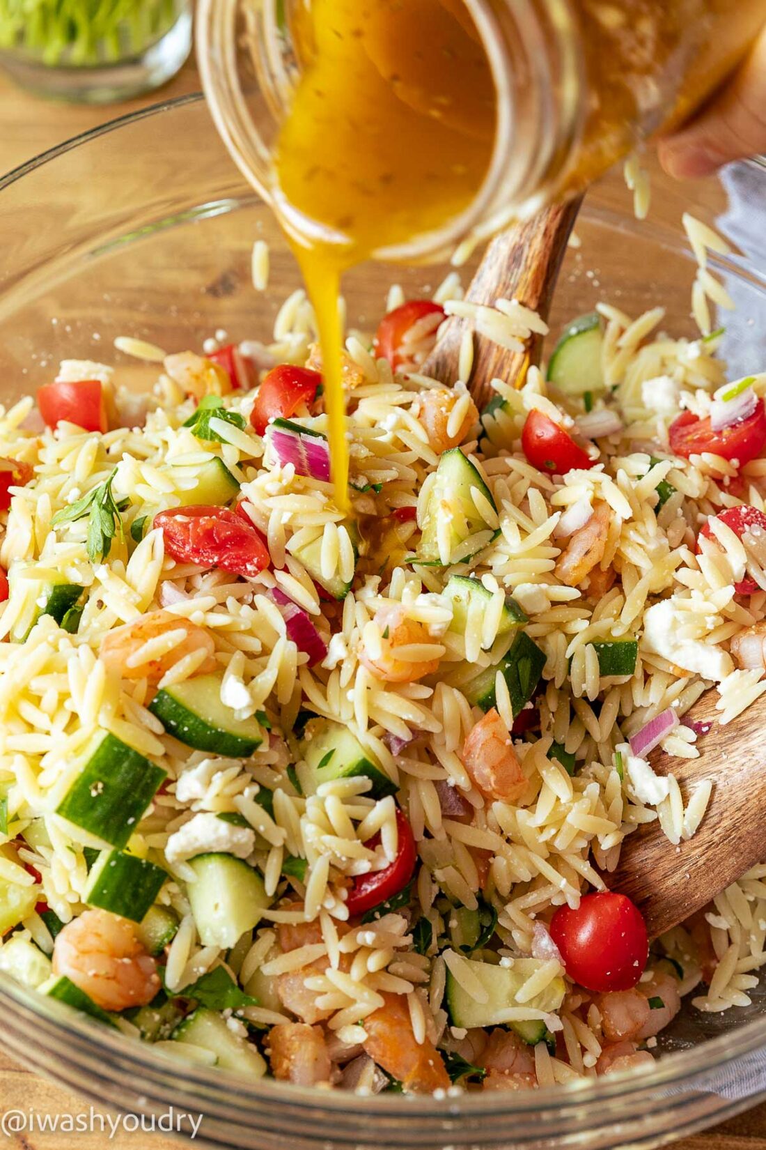 Pouring salad dressing over shrimp orzo pasta salad. 