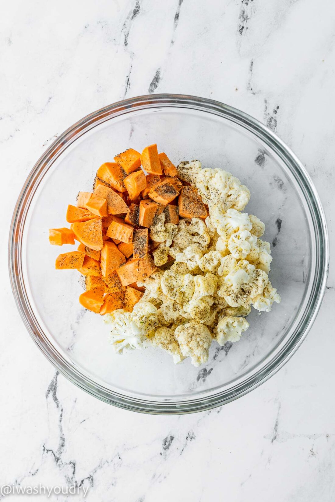 Raw sweet potato and cauliflower with spices in a transparent glass bowl. 