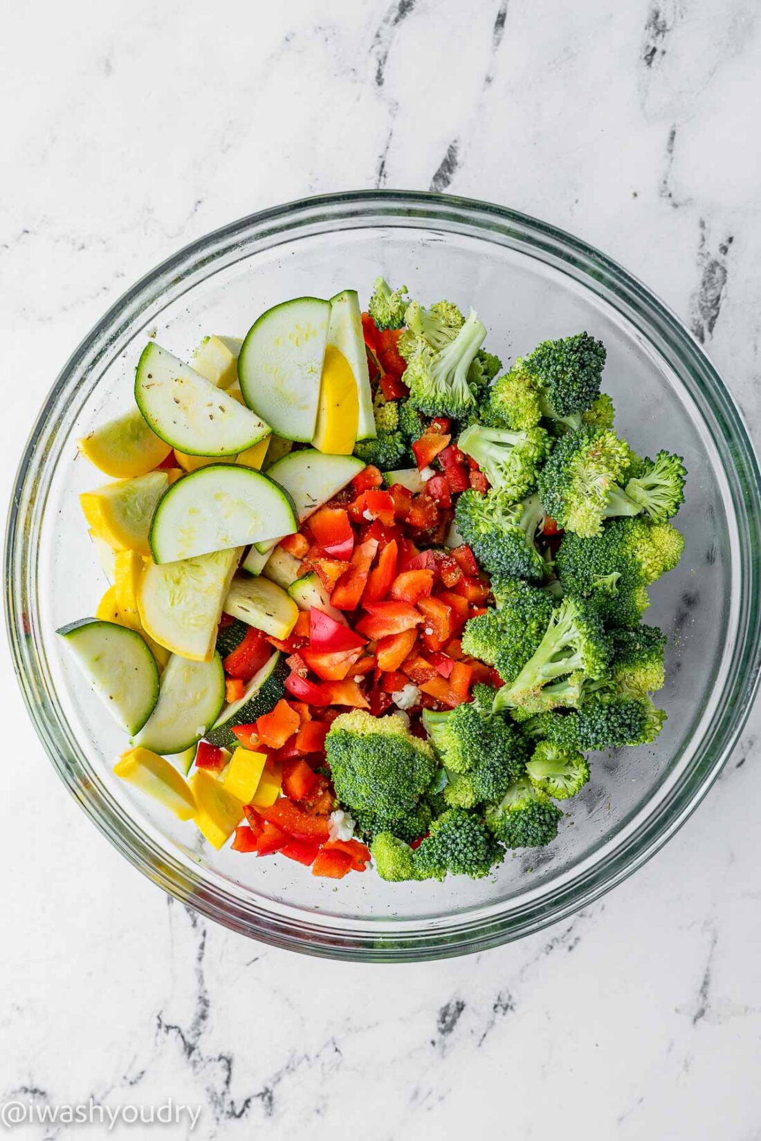 Raw zucchini, squash, broccoli, peppers in a glass bowl on marble. 