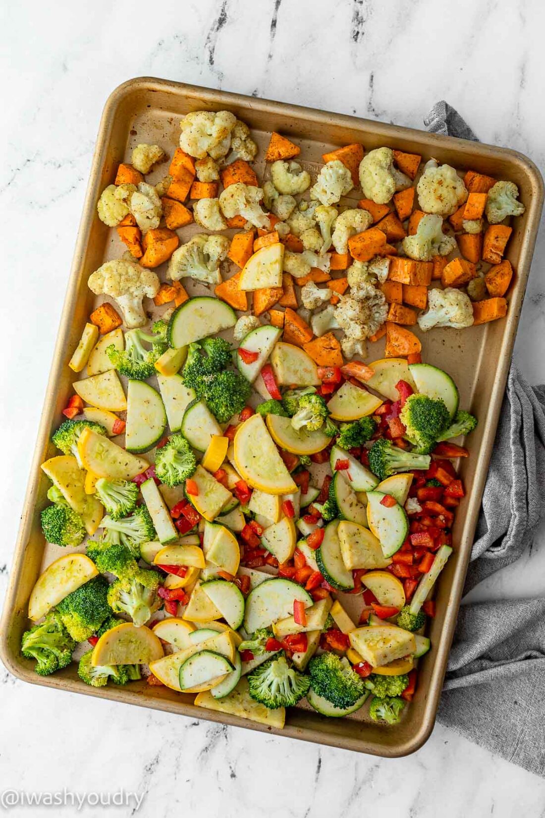 Raw zucchini, squash, bell pepper, and broccoli on pan with roasted sweet potatoes and cauliflower. 