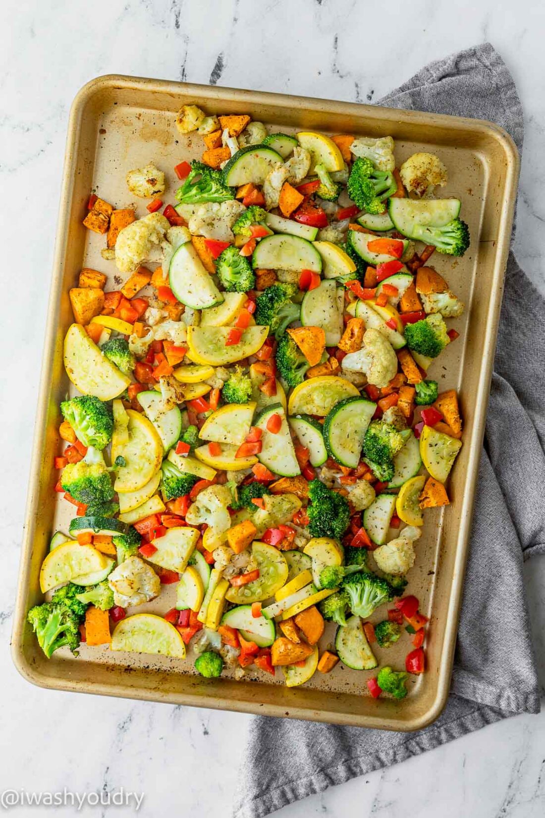 Overhead view of roasted rainbow vegetables on metal pan with dishtowel. 
