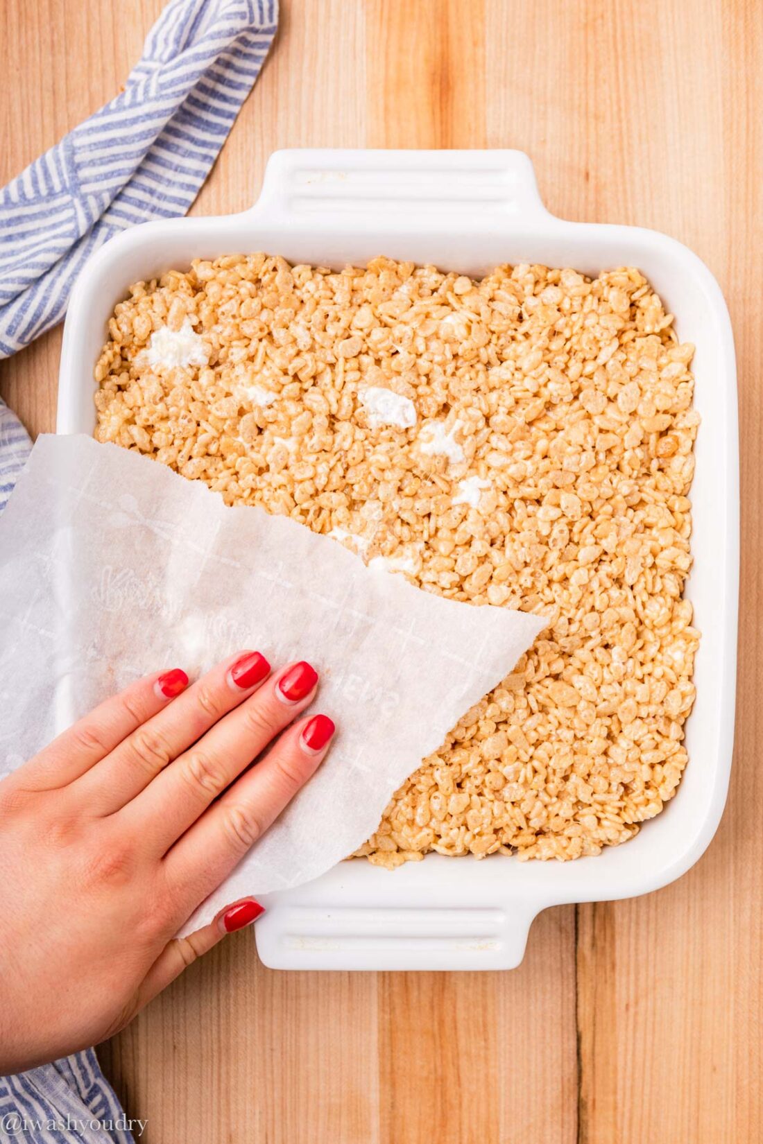 pressing cereal treats into pan with parchment paper.
