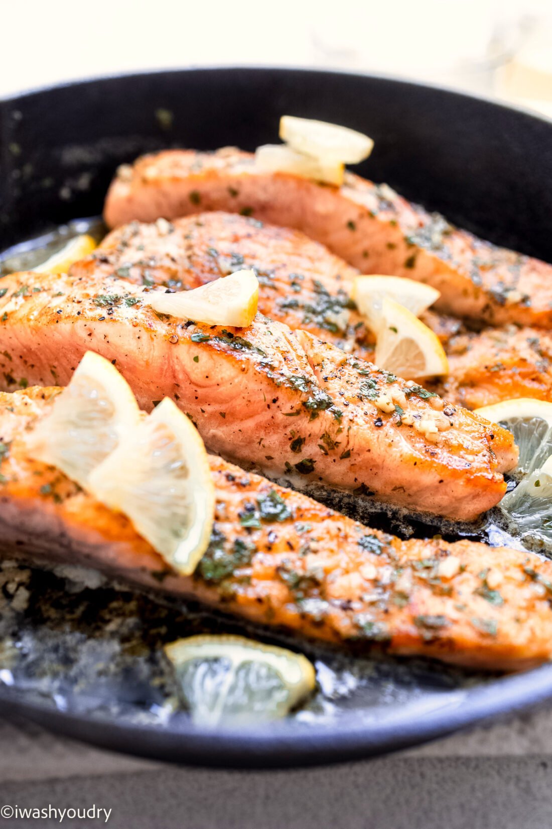 Slices of salmon cooked in a metal pan with lemon slices.