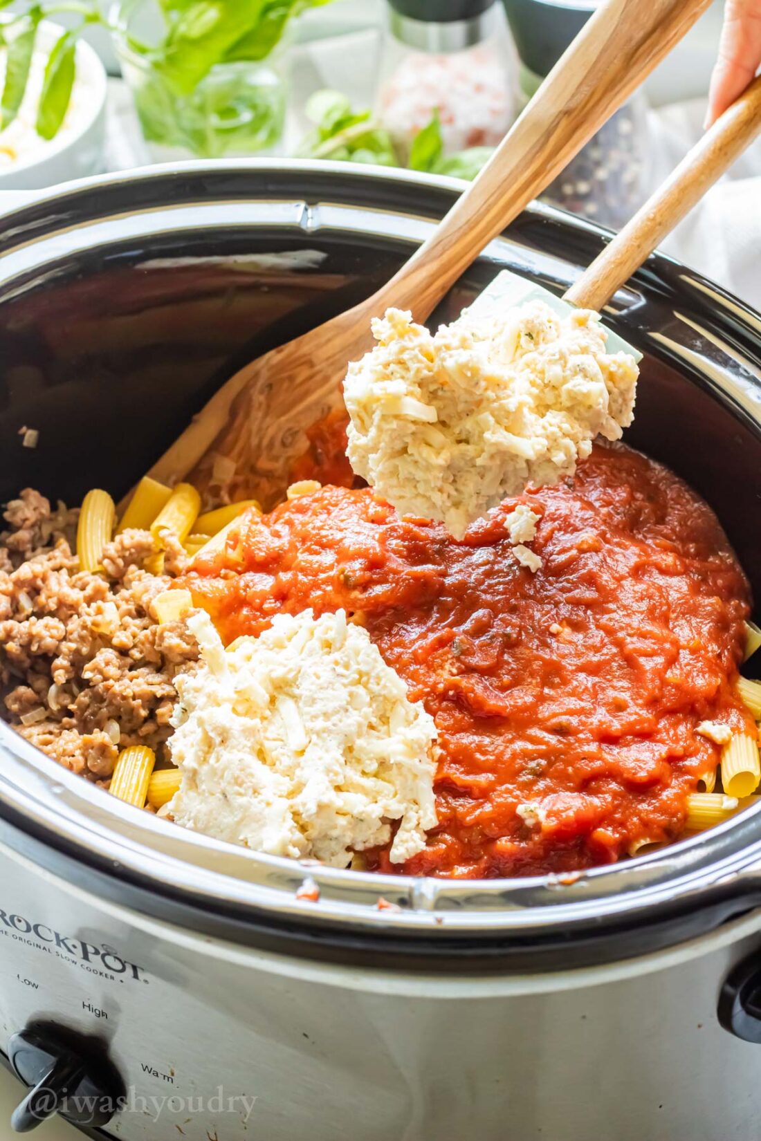 Spooning ricotta mixture into slow cooker of marinara and dry ziti noodles. 