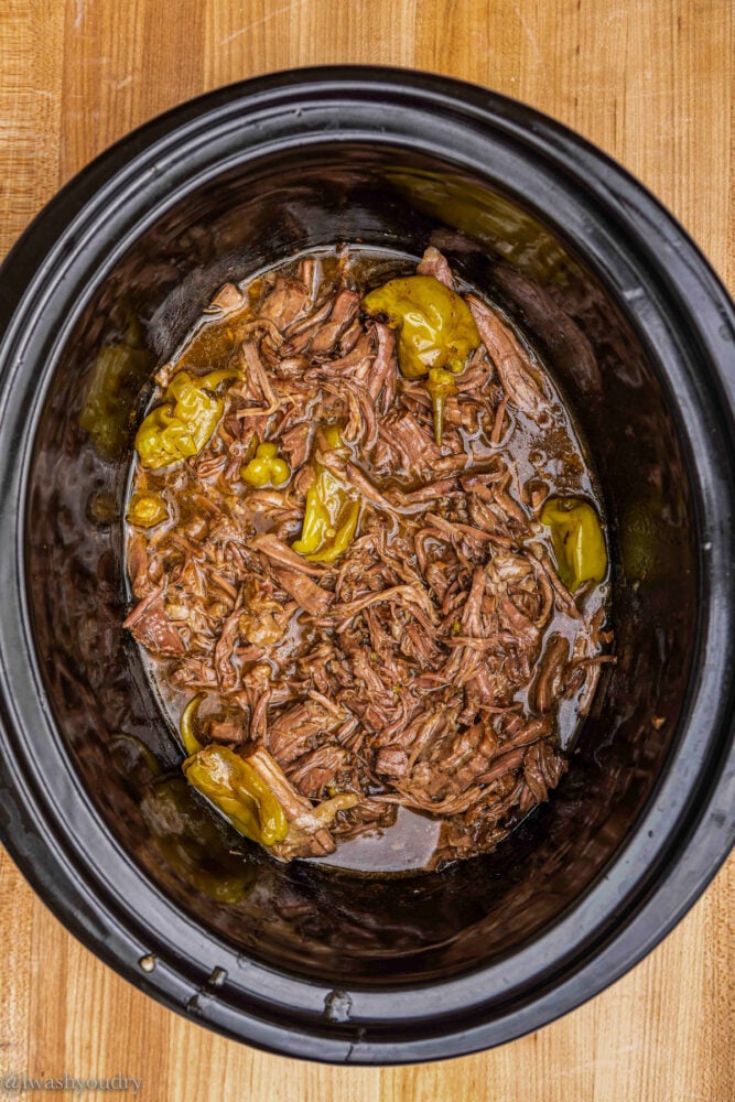 black slow cooker with shredded beef and peppers