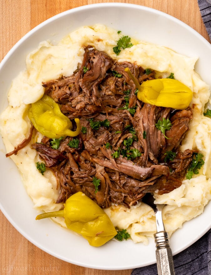 white plate with pot roast and mashed potatoes with peppers.