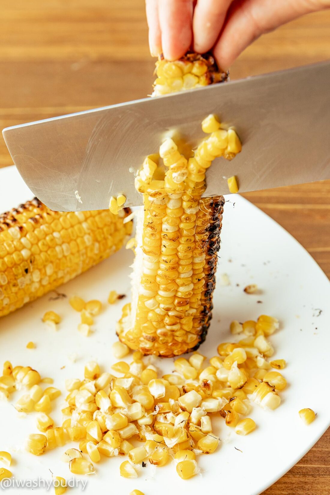 slicing grilled corn off cob with knife.