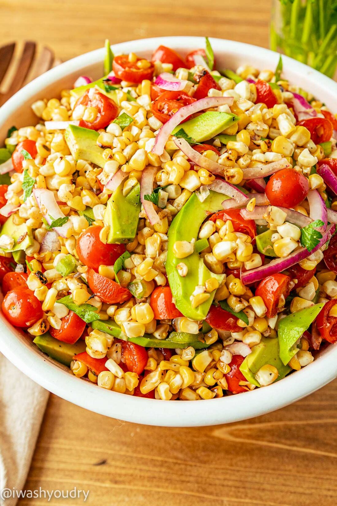 white bowl with corn, tomatoes and avocado with purple onion.