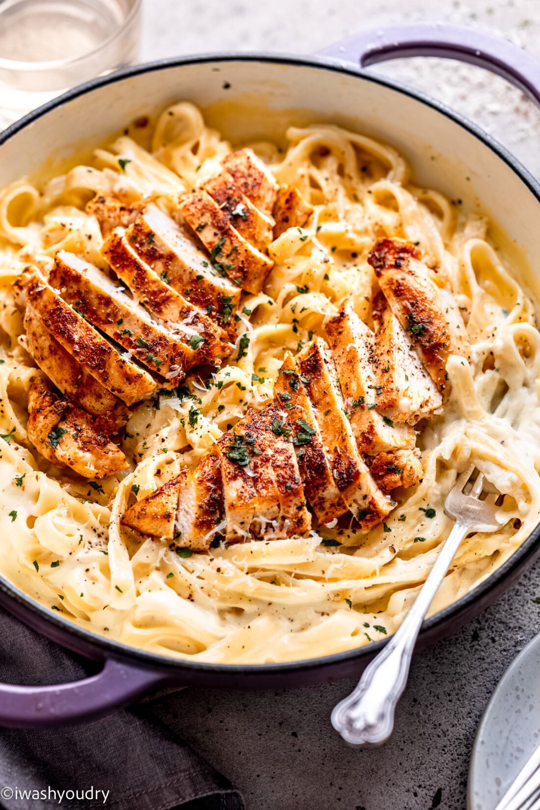 Cooked chicken in pan of noodles and alfredo sauce. 