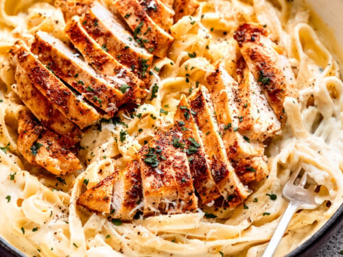 Cooked chicken in pan of noodles and alfredo sauce.