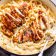 Cooked chicken in pan of noodles and alfredo sauce.