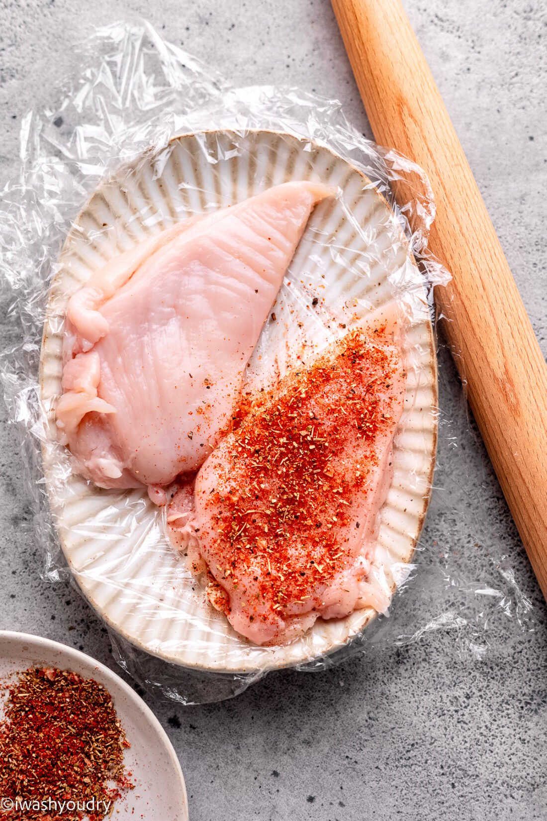 Raw chicken with seasoning on white plate plastic wrap with rolling pin. 