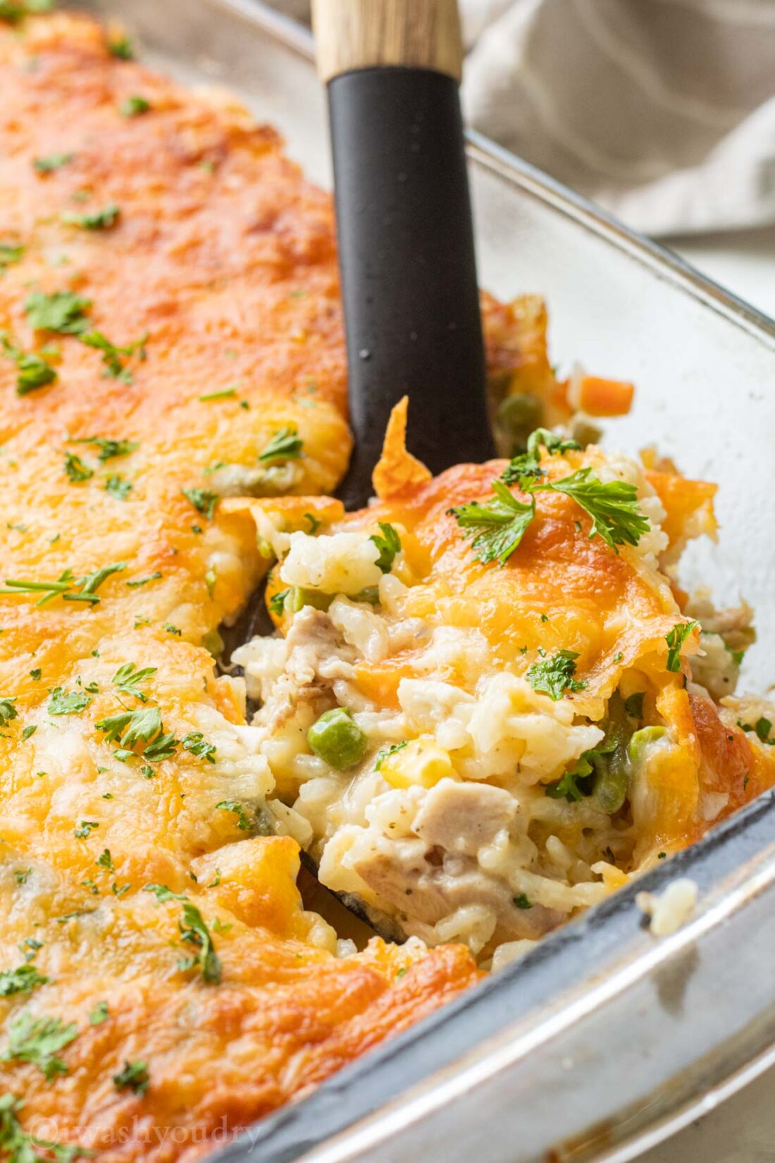 Black spoon of cooked chicken and rice casserole in glass pan. 