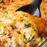 Baked chicken and rice casserole on black spoon in glass pan.