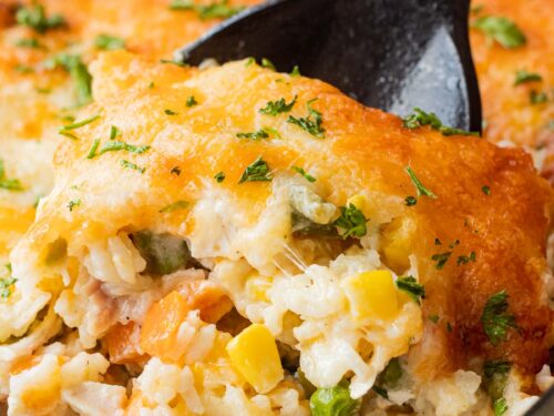 Baked chicken and rice casserole on black spoon in glass pan.