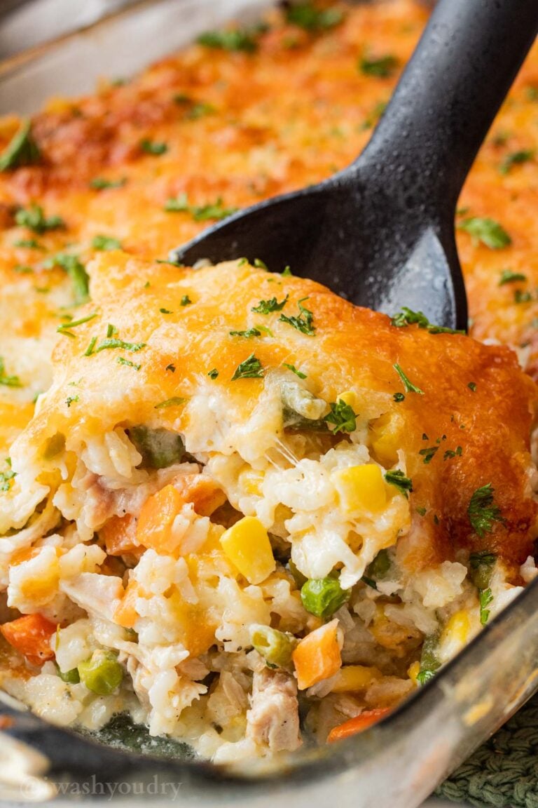 Baked chicken and rice casserole on black spoon in glass pan.
