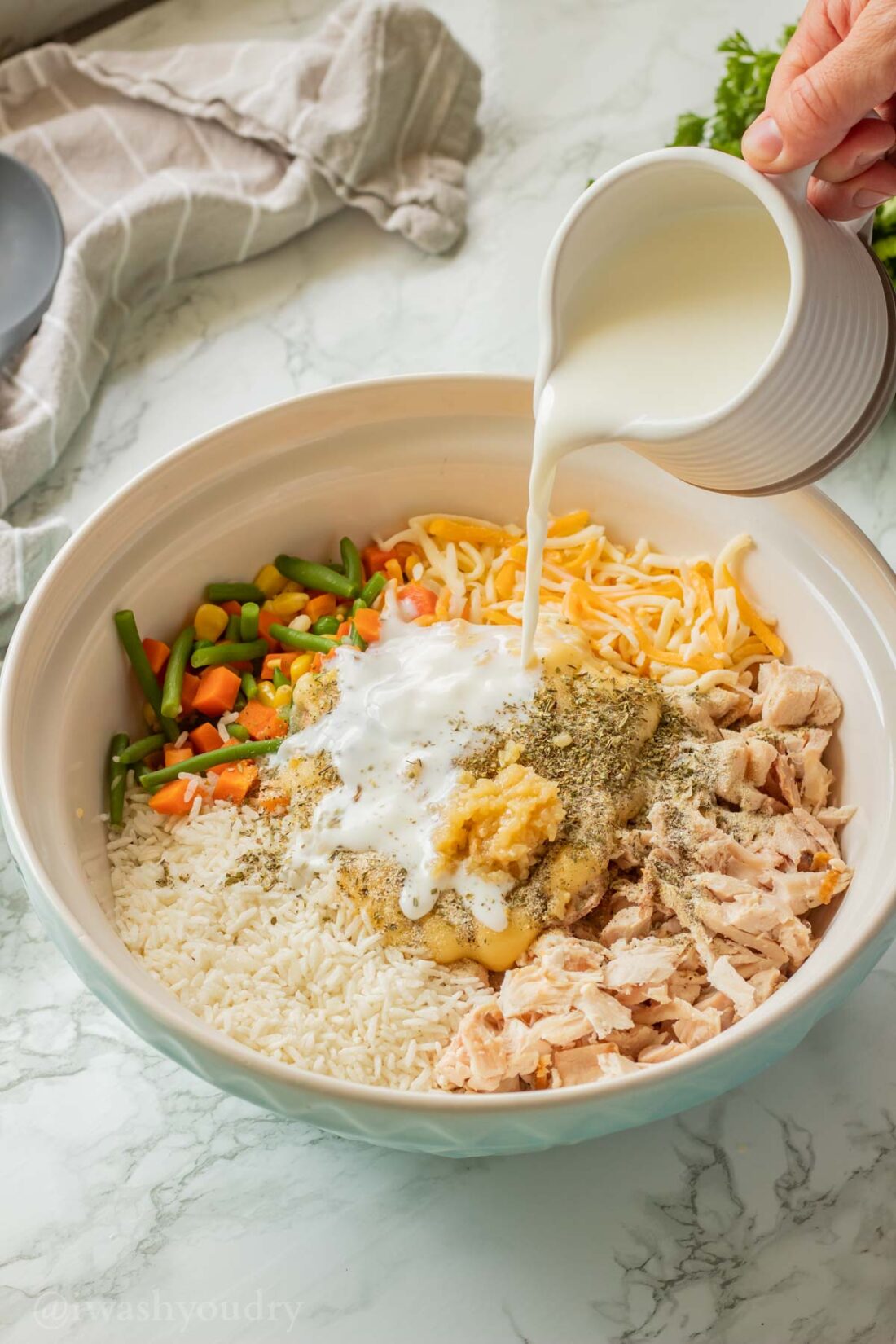 Pouring milk into bowl of creamy chicken and rice ingredients. 