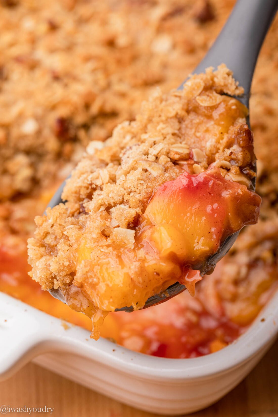 Spoonful of white baked peach crisp on top of a baking dish. 
