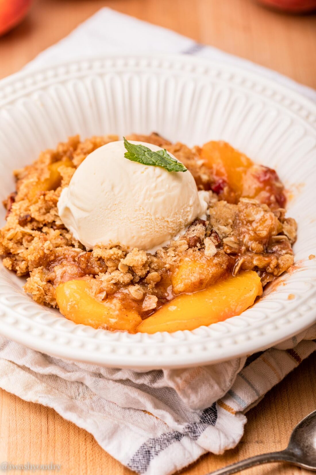Baked Peach Cristp in white bowl on dish towel.