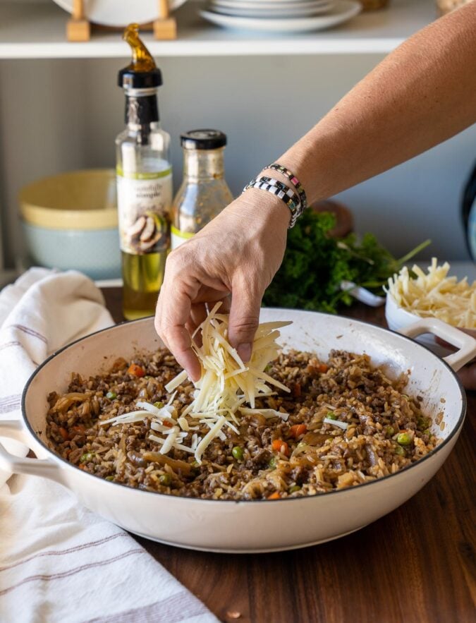 hand with cheese over white pan with rice