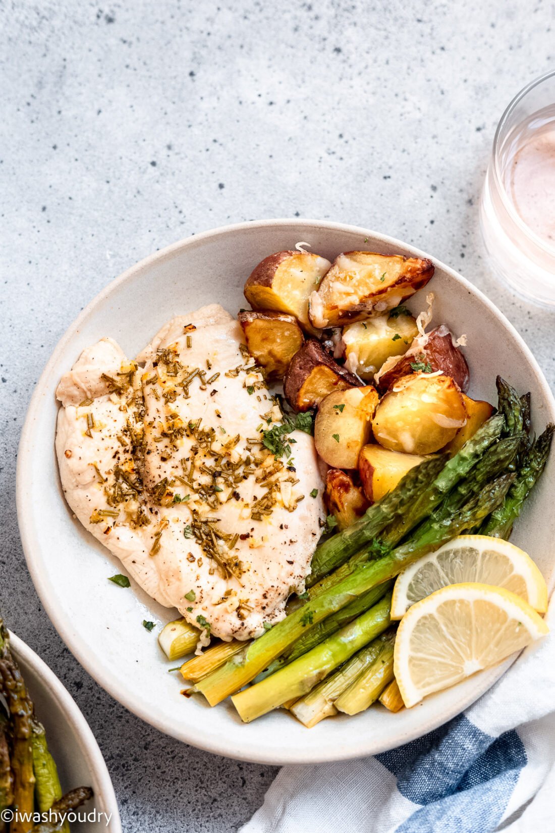 Baked lemon garlic chicken with potatoes, asparagus and lemon slices on a white plate. 