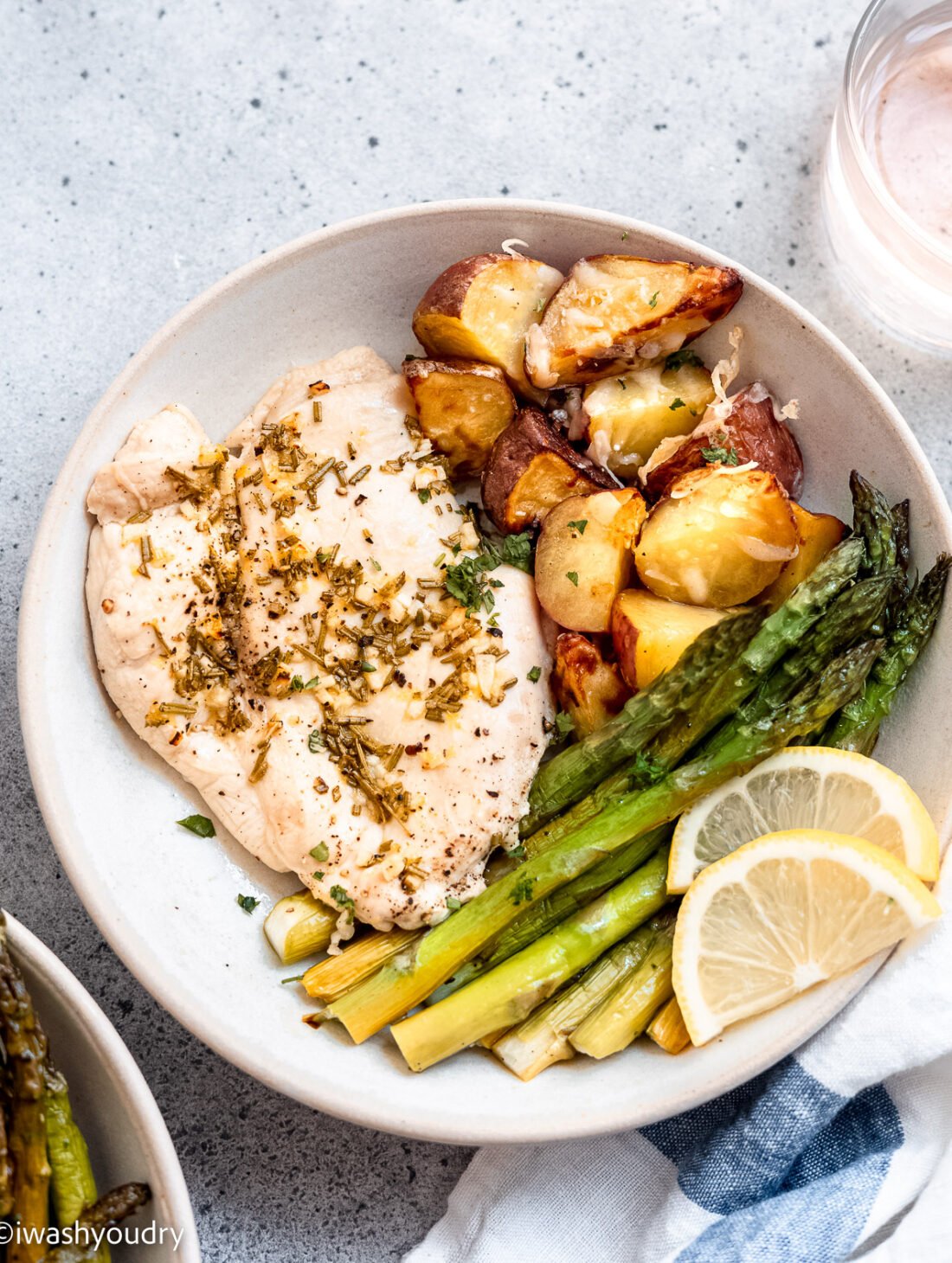 Baked lemon garlic chicken with potatoes, asparagus and lemon slices on a white plate.