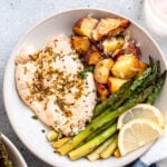 Baked Lemon Garlic Chicken with potatoes, asparagus, and lemon slices on white plate.