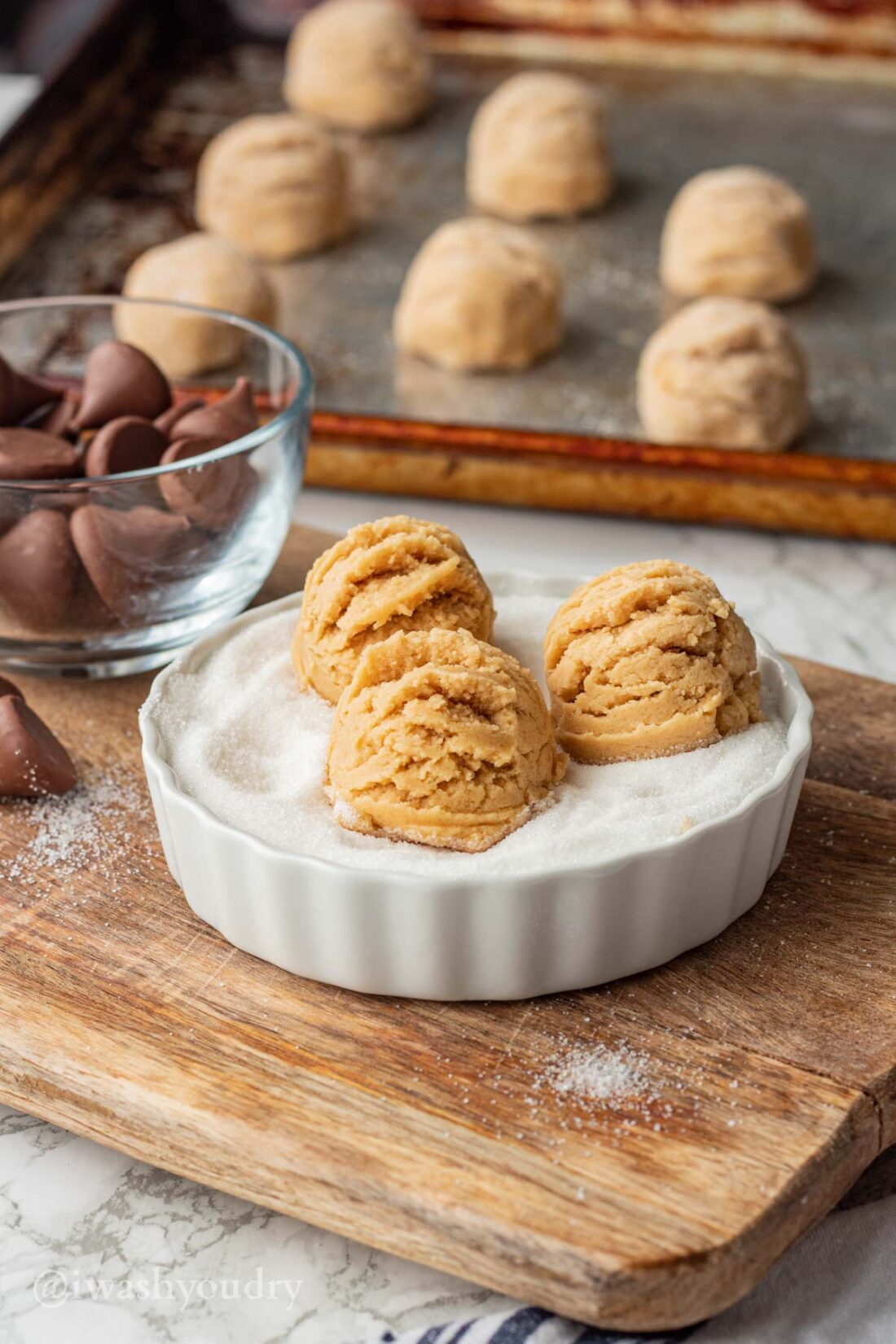 3 raw peanut butter cookie dough balls in white dish of sugar. 