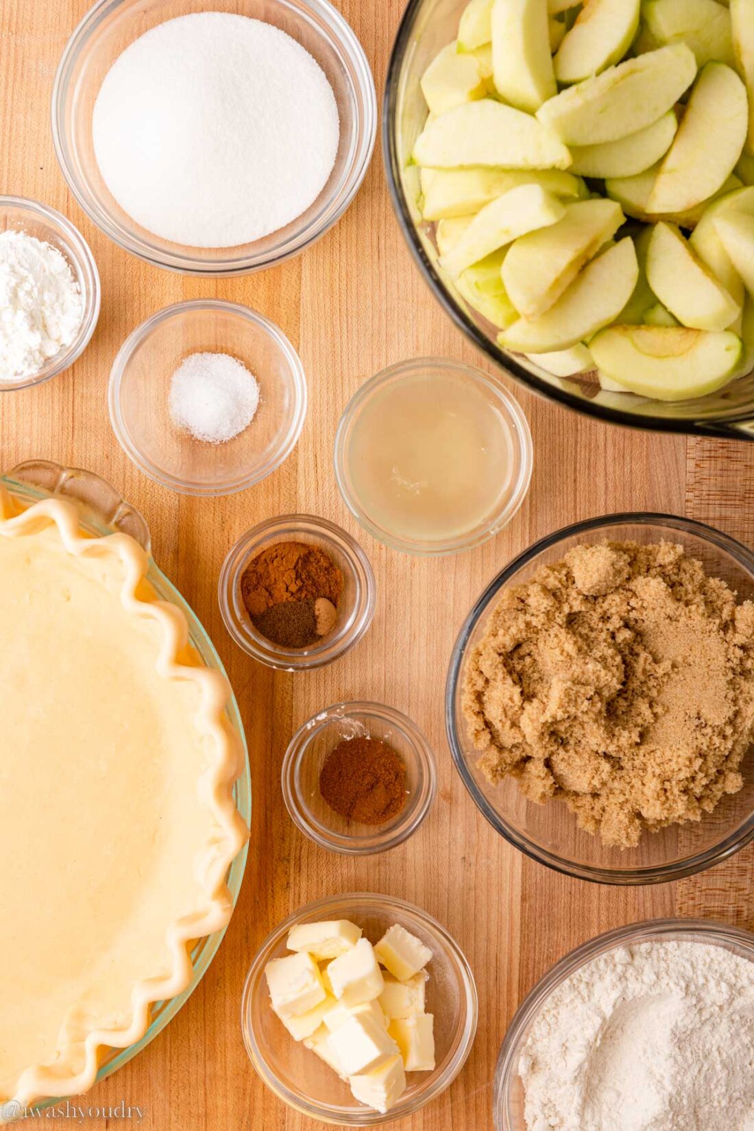 Ingredients for dutch apple pie in glass bowls on wood countertop. 