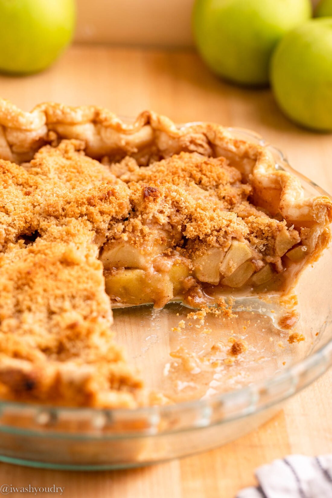 Baked dutch apple pie with slices removed and green apples in background. 