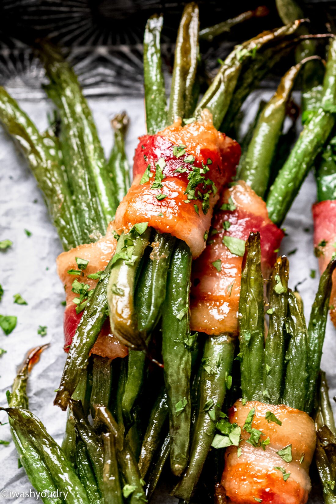 a pile of green beans wrapped in bacon with parsley on top.