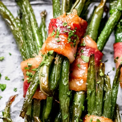 a pile of green beans wrapped in bacon with parsley on top.