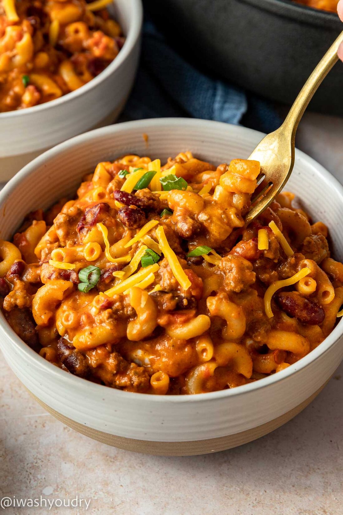 forkful of chili mac with cheese and green onions in white bowl.