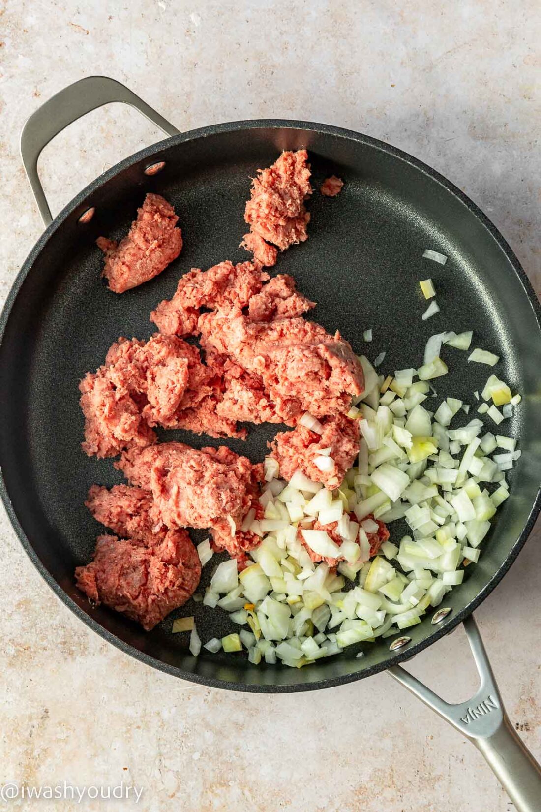 uncooked ground beef in skillet with onion on white surface.