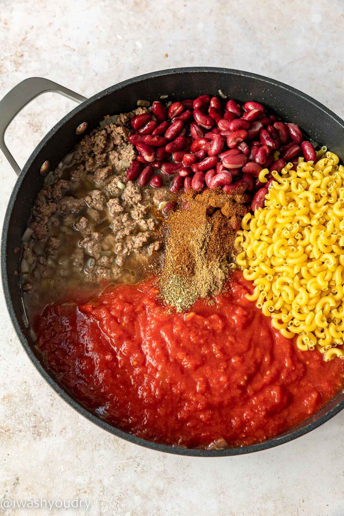 Ingredients for cheesy chili mac in skillet with dry noodles.