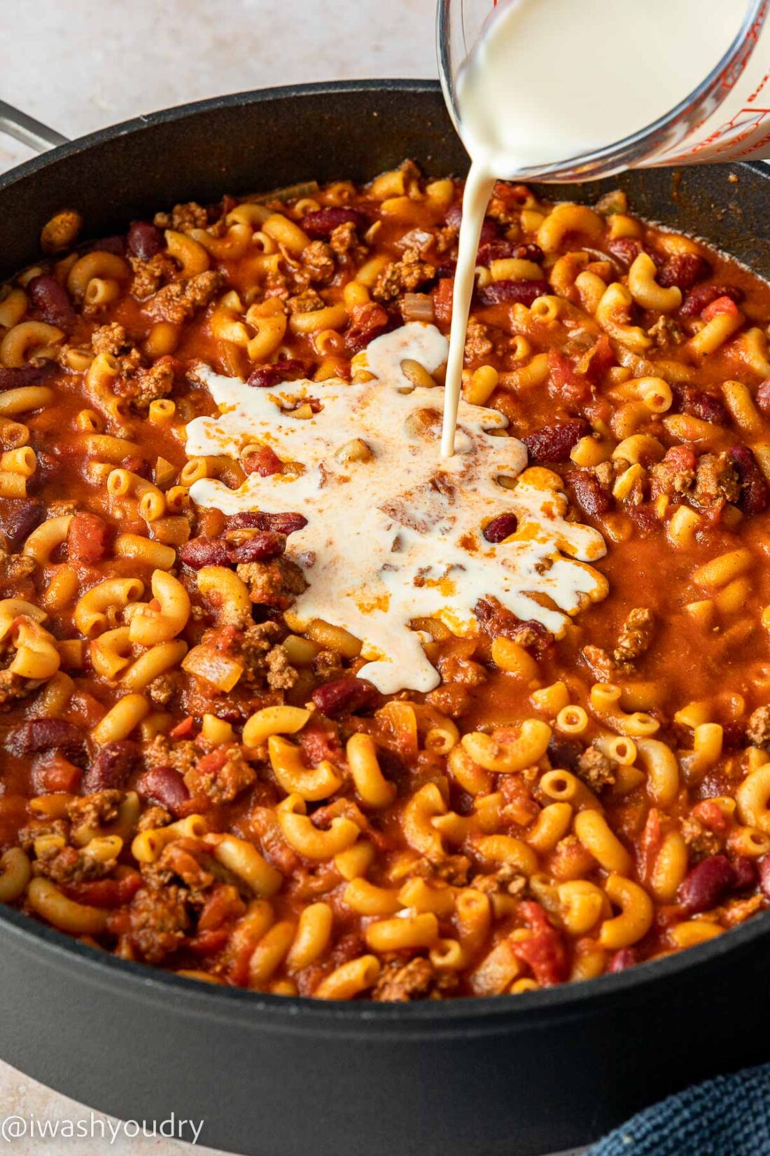 pouring evaporated milk into chili macaroni.