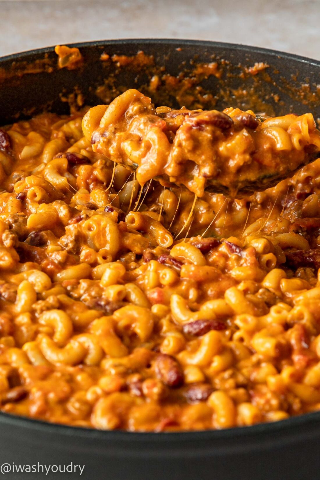 Cheesy scoop of chili mac in pan with wooden spoon.