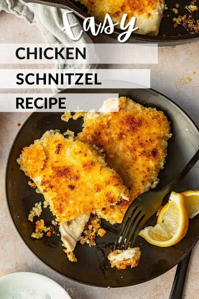 Cooked chicken schnitzel on black plate with lemon.