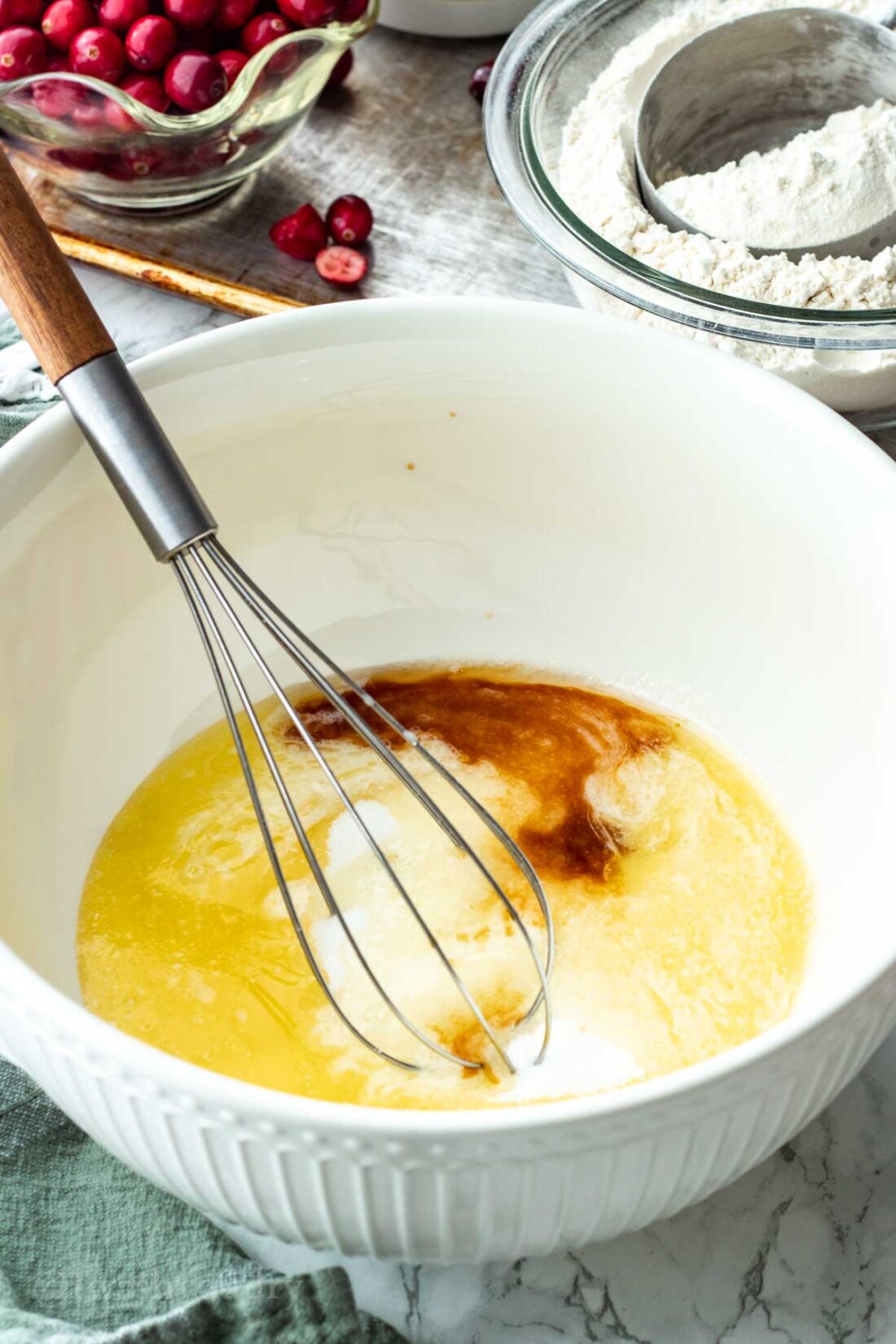 Butter, sugar, and vanilla in a white mixing bowl with whisk. 