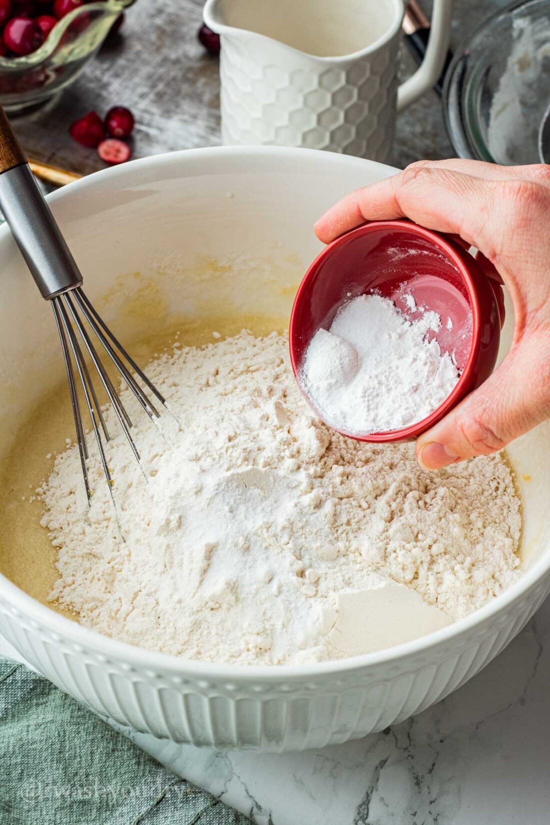 Pouring red dish of dry ingredients into white mixing bowl. 