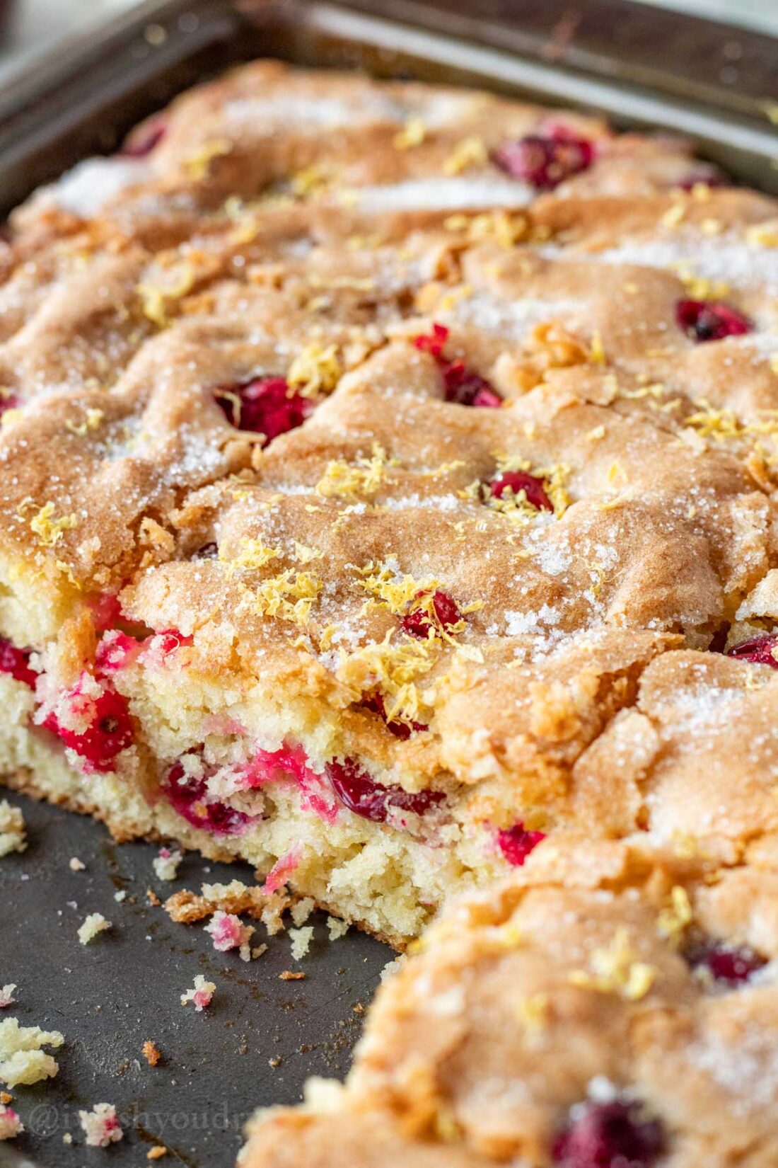 Sliced cranberry breakfast cake in metal pan with slices removed. 