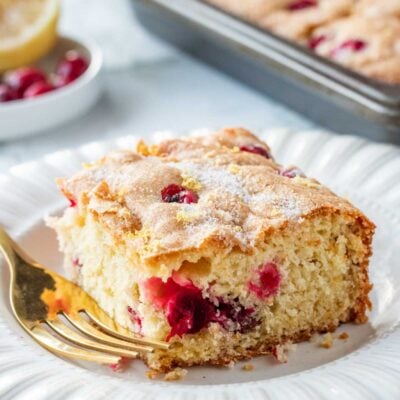 Sliced of baked Cranberry Buttermilk Cake on white plate with gold fork.