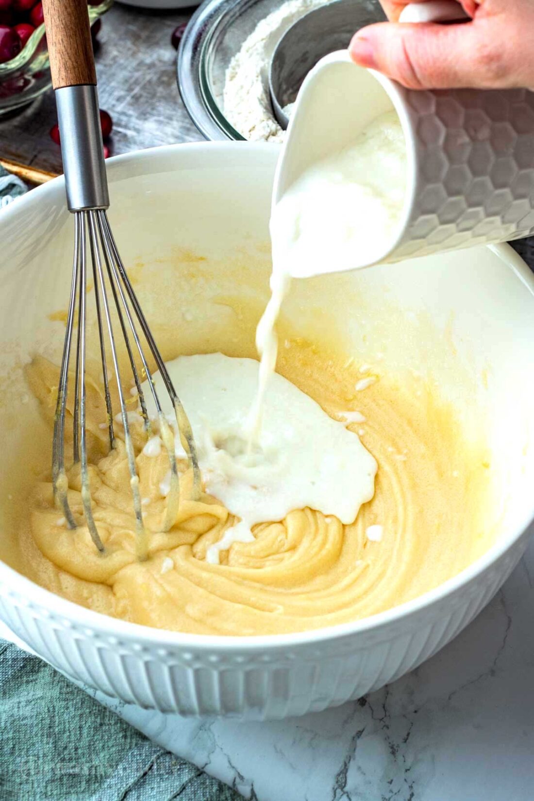 Pouring buttermilk from white pitcher into mixing bowl with whisk. 