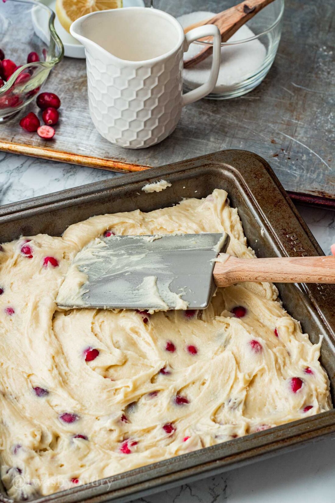 Spreading raw buttermilk cranberry cake batter into metal pan with spatula. 
