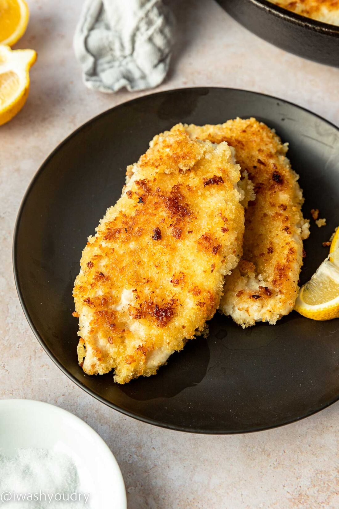 Cooked Chicken Schnitzel on a black plate with lemon wedge. 
